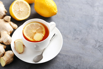 Cup of tea with ginger root and lemon on grey wooden table