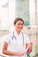 Happy smiling beautiful doctor stands and keeps folder in hands outdoor