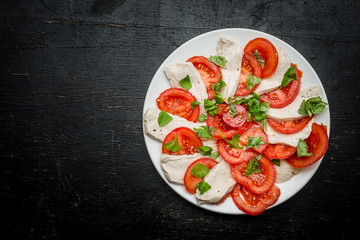 vegan mozarelle with tomatos and spinach on a plate on a dark wooden surface - table top