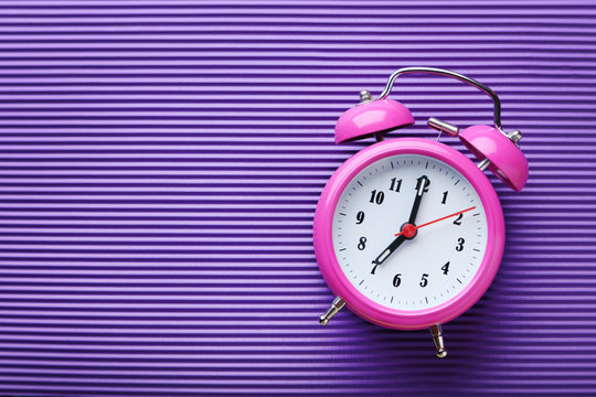 Pink alarm clock on purple background
