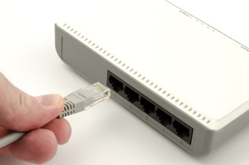 A close-up view of a finger's hand connecting a gray lan cable into the router on a white background