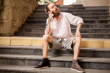 Stylish tattoed and bearded guy posing outdoor in the city