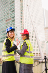 Portrait of two young, successful women architects who stand together and keep the folder with some documents in hands, one of them shows sign ok her fingers, outdoors