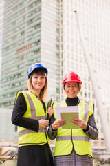 Portrait of two young, smiling women architects who stand together and keep the folder with some documents in hands, outdoors