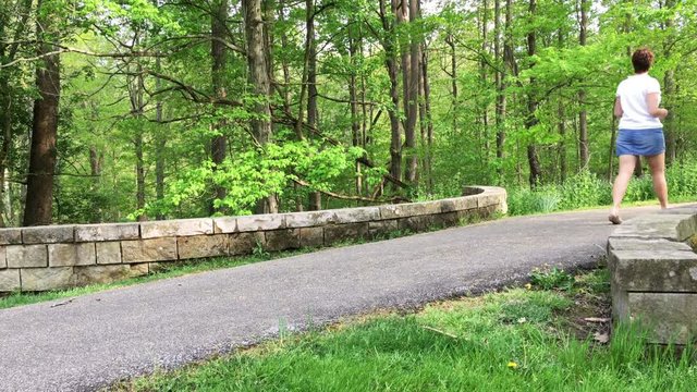 Woman walks over stone bridge during nature trail in summer