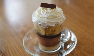 Banoffee pie dessert in glass cup with spoon on wooden table.