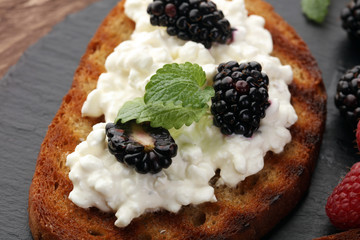 Bread with cheese cream and blackberries and raspberries for lunch table. Sharing antipasti on party or summer picnic time over wooden rustic background.