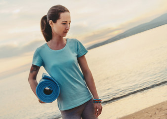 Woman with yoga mat standing on beach