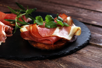 Bread with slices jamon serrano for lunch table. Sharing antipasti on party or summer picnic time over wooden rustic background.