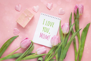 Mothers Day message with notepad, tulips and gift box on a pink background.