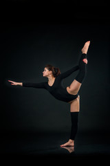 Sporty gymnastics woman stretching on One leg on black background