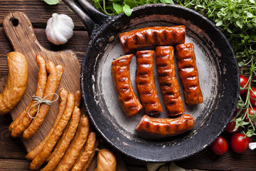 Roasted sausage in a pan and raw sausage on wooden board