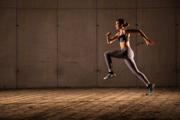 Young woman runner is seen running in an abandoned hall. Running is a good exercise for cardio vascular system and general health and weight control.