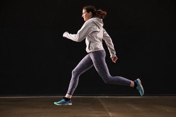Fototapeta na wymiar Young woman runner is seen running in an abandoned hall. Running is a good exercise for cardio vascular system and general health and weight control.