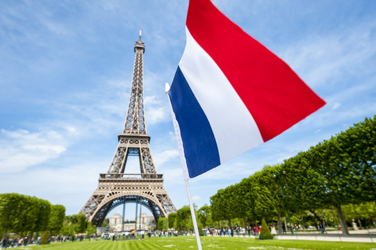 Tricolour French flag flying in blue sky in front of the Eiffel Tower in Paris, France