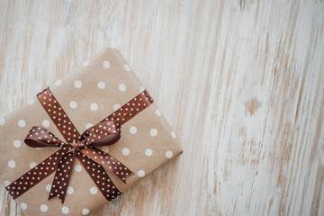 Box in craft paper, eco paper on the wooden table. Top view. Brown paper wrapped gift box with satin ribbon bow on a old rustic wood background. Background for your design. Retro filter