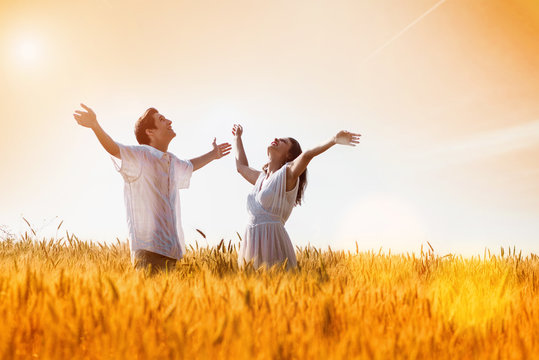 Happy, young couple with arms outstretched ,enjoying in the wheat field, summer season. Sunset light, flare light, copy space - Powered by Adobe
