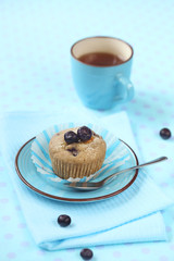 Blueberry Muffin on blue plate and cup of tea, on light blue background.