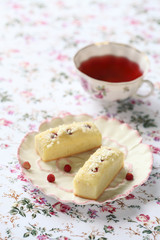 White Chocolate Financiers with Wild Strawberries and cup of fruit tea, on white floral background.
