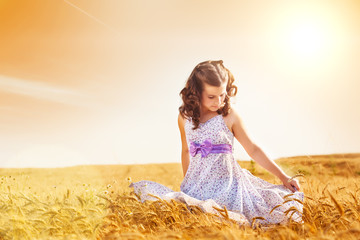 Little girl holding her dress in a wheat field, flare light, copy space