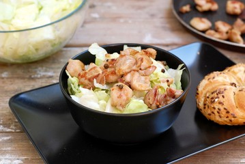 Fresh salad from lettuce and pieces of fried chicken in black bowl