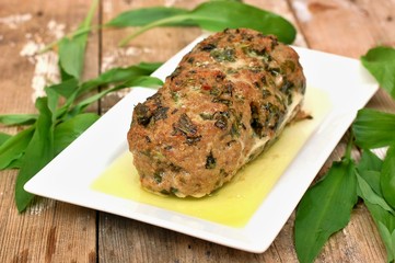 Meat loaf with fresh green buckrams leaves on white plate on wooden background