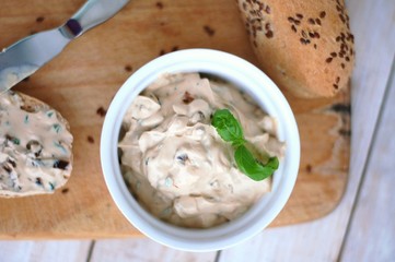 Bread with spread from basil, sundried tomato and basil in white bowl on wooden background
