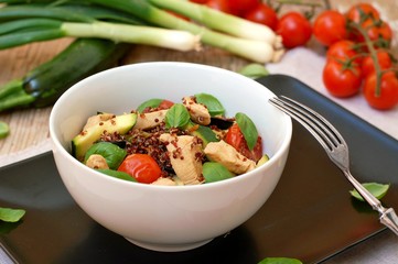 Gluten free food with red quinoa, chicken fillet, tomato,zucchini, olive ,basil leaves and spring onion in white bowl on wooden background