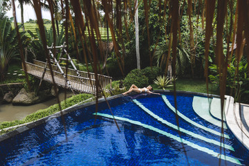 Woman relaxing in pool with deep blue water in tropical Bali garden. Spa organic skin care, healthy lifestyle, jacuzzi
