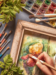 Naklejka premium Brushes, acrylic and watercolor paints, a picture in a frame and a canvas, tools for the artist's creativity on a dark background in a vintage style