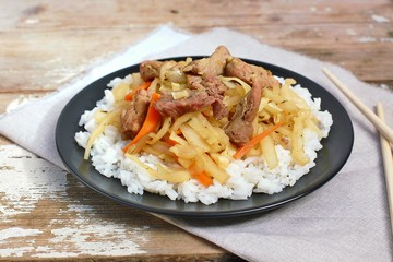 Chinese food with rice,carrot, cabbage and meat on black plate on wooden background