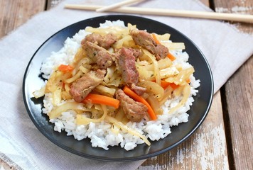 Chinese food with rice,carrot, cabbage and meat on black plate on wooden background