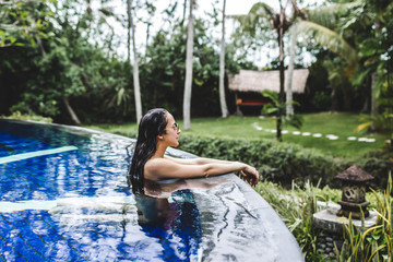 Woman relaxing in pool with deep blue water in tropical Bali garden. Spa organic skin care, healthy lifestyle, jacuzzi - obrazy, fototapety, plakaty