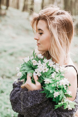 Blonde girl poses with bouquet of white flowers in the forest