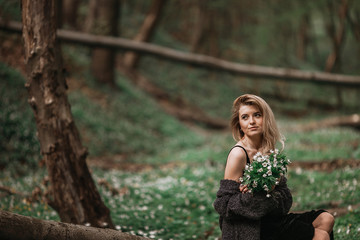 Fototapeta na wymiar Woman holds bouquet of white flowers before her chest posing in the forest