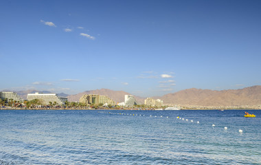 View on the Red Sea and hotels from central beach of Eilat - famous Israeli city with beautiful sandy beaches, hot sun and clear blue skies, surrounded by stunning mountains and desert scenery