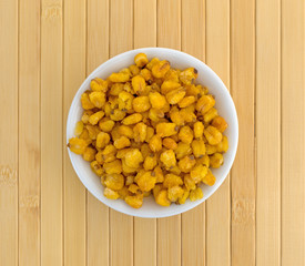 Top view of toasted corn nuts in a small white bowl on a wood place mat.
