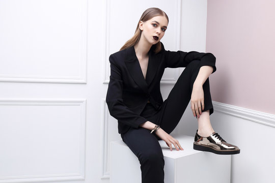 High fashion portrait of young elegant woman in black suit and loafers.