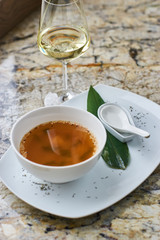 Japanese cuisine. Miso soup in white ceramic bowl served with green leaf, sppon and glass of white wine on marble table.