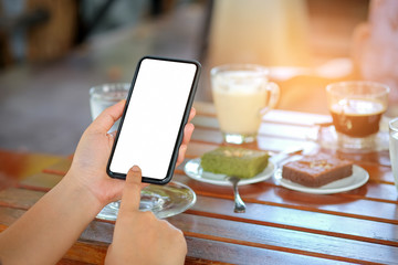 Smart phone in hand with coffee and cake on table.