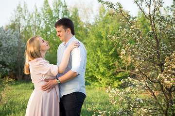 Fototapeta premium Young parents in a spring park at sunset. Pregnant woman.