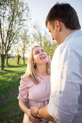 Fototapeta premium Young parents in a spring park at sunset. Pregnant woman.