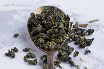 Leaves of green tea in a spoon on a white background. Tea in an antique spoon.