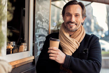 Joyful middle-aged businessman drinking latte on street