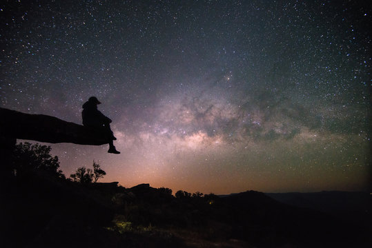 Woman sits on stone lodge and look night sky stars with milky way background