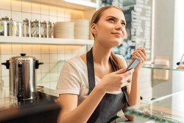 Thoughtful waitress using phone in cafe