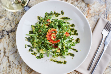 Salad with couscous, cherry tomatoes, avocado and mozzarella served on white plate. Salt shaker, pepper-castor and knife and fork on napkin on marble table