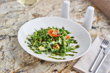 Salad with couscous, cherry tomatoes, avocado and mozzarella served on white plate. Salt shaker, pepper-castor and knife and fork on napkin on marble table