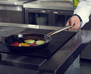 The chef of the restaurant prepares fried vegetables in the pan in the kitchen, filtered image