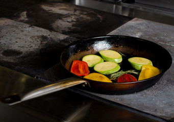 The chef of the restaurant prepares fried vegetables in the pan in the kitchen, filtered image